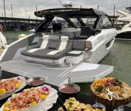 A luxury yacht docked at a marina with seafood and cheese platters arranged on a table in the foreground.