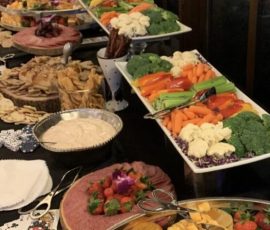 A long table with assorted cheeses, crackers, fruits, vegetables, dips, and meats arranged on trays and platters.