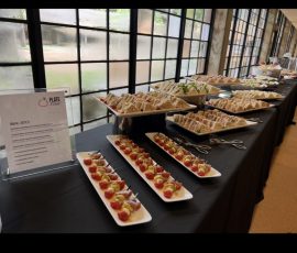 A buffet table with assorted sandwiches and appetizers on trays, set near large windows with natural light.