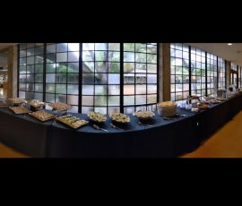 Long buffet table with assorted snacks and appetizers in front of large glass windows in a modern indoor venue.