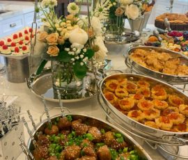 Buffet table with trays of meatballs, pastries, and other appetizers, decorated with fresh white and beige flowers.