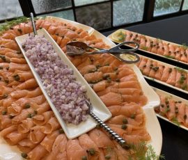 Plates of sliced smoked salmon garnished with capers and dill, served with chopped red onions and utensils.