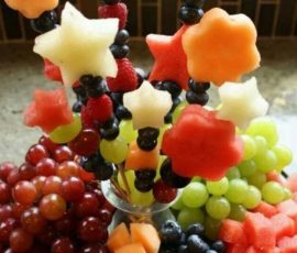 Fruit arrangement with grapes, cantaloupe, and star-shaped and flower-shaped melon skewers in a glass vase.