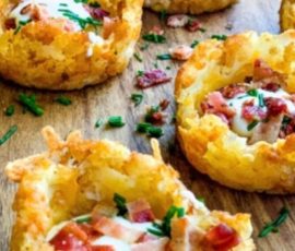 Mini hash brown nests filled with chopped bacon, cheese, and herbs arranged on a wooden surface.